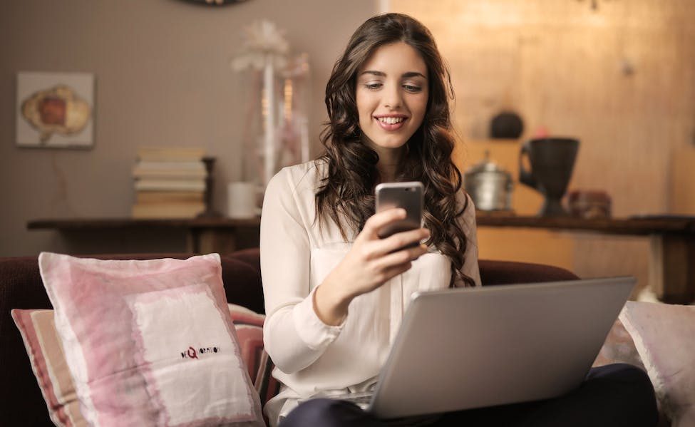 femme souriante devant PC et téléphone